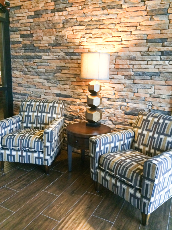 stone wall in lobby with geometric fabric on lounge chairs round table and gold lamp design 